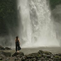 Woman pauses at foot of waterfall by daria lisovtsova
