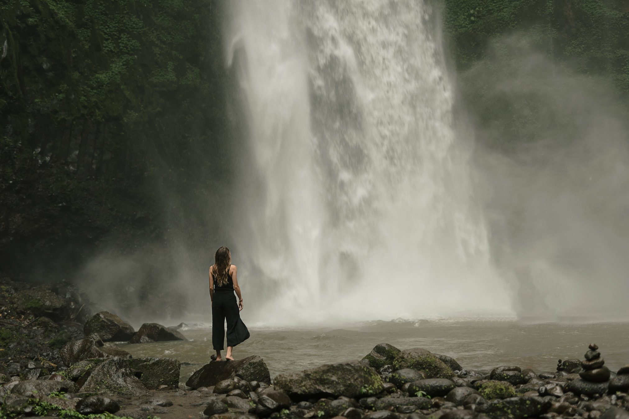 Woman pauses at foot of waterfall by daria lisovtsova - Ubuntu Budgie 26.04 Wallpapers - Official Indigo Collection